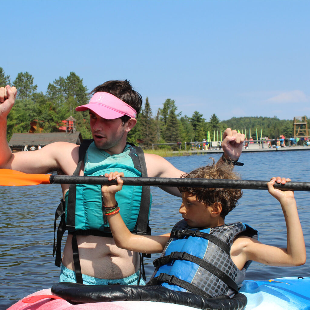 leader in training program, older camper helping younger camper in kayak