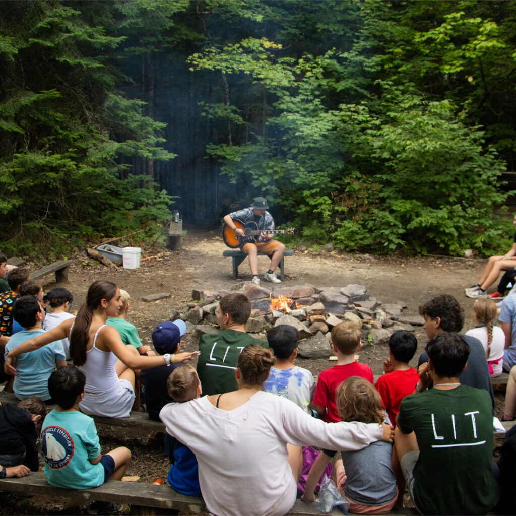 man playing guitar for campers outside